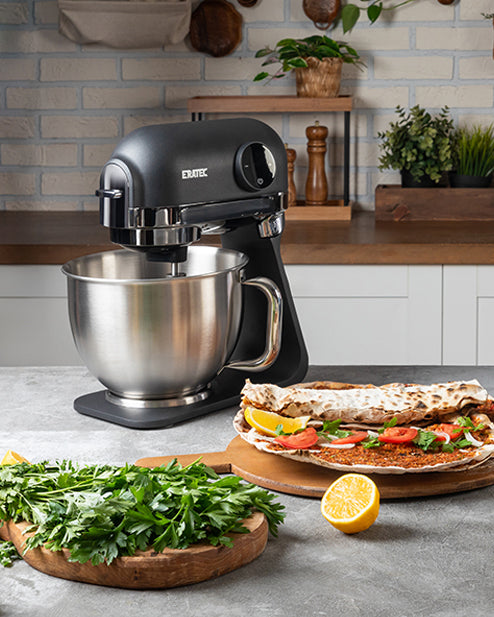 Küchenmaschine mit Edelstahlschüssel in moderner Küche, frische Kräuter und Wraps auf Holzbrett