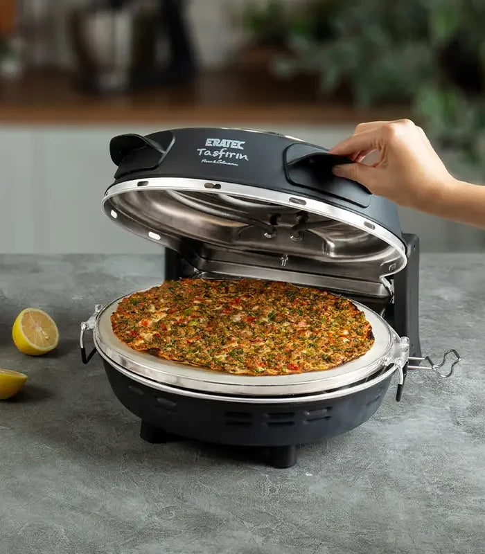 Elektrischer Steinofen mit geöffnetem Deckel, frische Lahmacun auf Backfläche, Zitrone daneben.